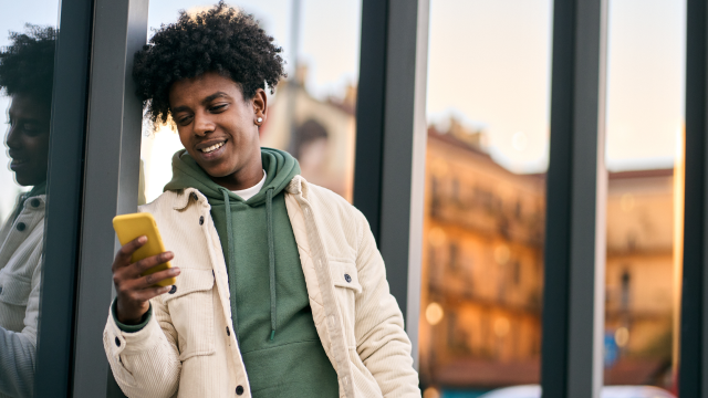 A man leans against a wall, looking at his phone.