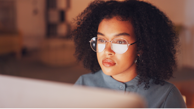A woman with glasses looks at her computer screen.