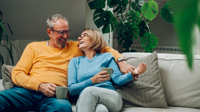 A couple sit on a sofa, laughing together.