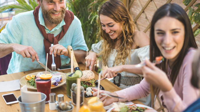 Three people sit at a table outside, happily eating brunch together.