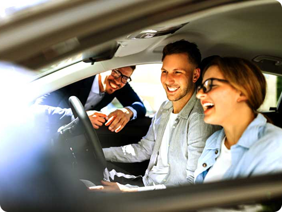 A smiling man and woman are looking at a new car with help from a car sales assistant