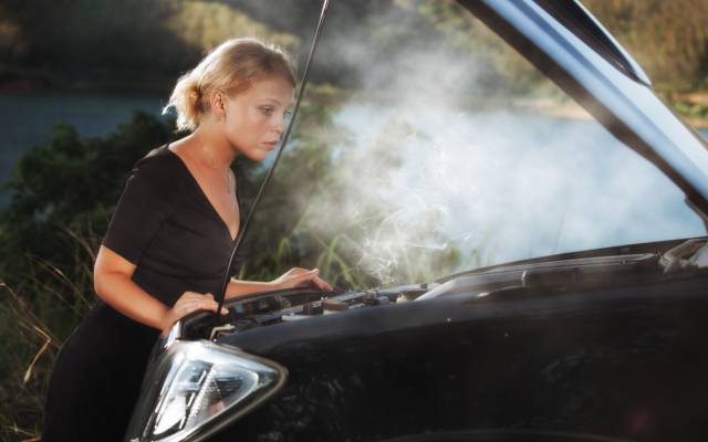 Woman looking at overheated engine with steam coming out