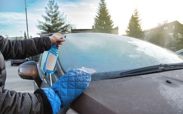 man with windscreen deicer and ice scraper