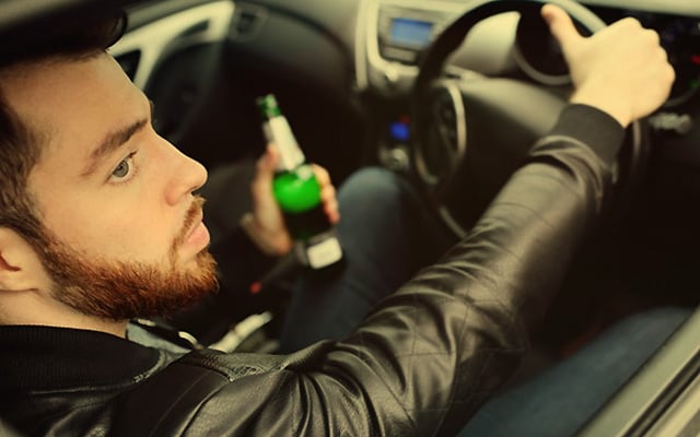 Man driving over the limit, holding a beer