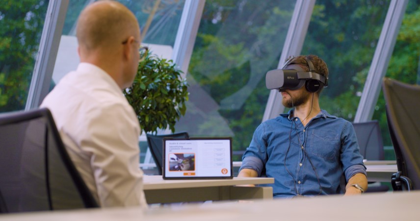 Trainee driving instructor with trainer seated in office wearing virtual reality headset