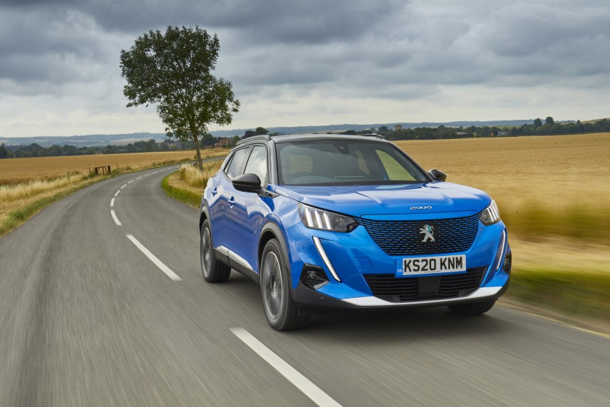 A blue Peugeot e-2008 driving alongside a wheat field