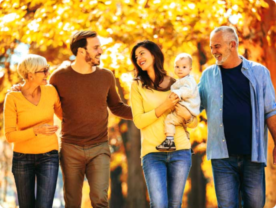 A smiling family walk arm-in-arm, with sunshine and trees in the background.