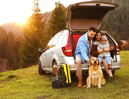 A family sit at the back of their car with the boot open, in a scenic setting.