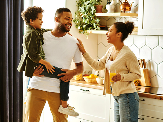 A family stands smiling and chatting in their kitchen.