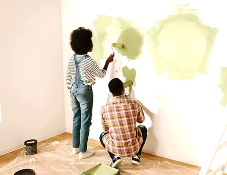 A man and a woman paint a wall green.