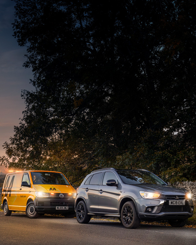 A yellow AA patrol van and silver car on side of road