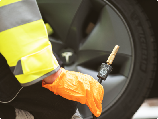 Person in a yellow high-visibility jacket and orange gloves inflating or checking the tyre pressure of a vehicle