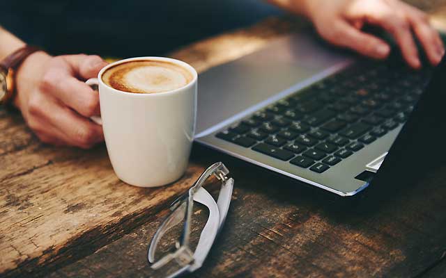 Hands using laptop with coffee and glasses on table