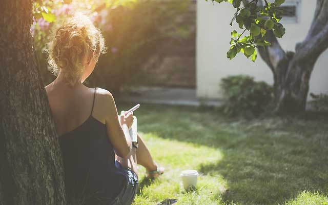 Woman sitting in a sunny garden while writing